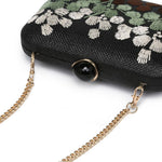 Black clutch with floral embroidery and gold chain strap on a white background