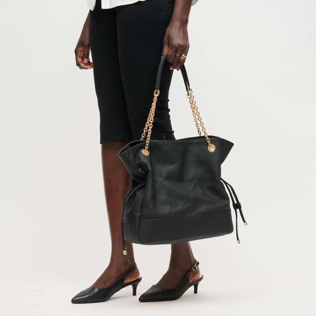Black handbag with gold chain handle held by a person on a white background