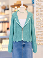 Kennedy Hoodie in teal featuring textured open knit, a full zipper with ring pull, hood with drawstrings, and cropped scalloped hem, styled with denim at Ardor Boutique.