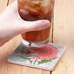 Hand holding a glass of iced tea on a floral coaster with a wooden background