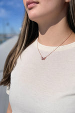 Close-up of a person wearing a delicate necklace with a butterfly pendant against a blurred outdoor background.