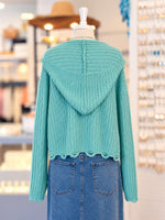 Kennedy Hoodie in teal featuring textured open knit, a full zipper with ring pull, hood with drawstrings, and cropped scalloped hem, styled with denim at Ardor Boutique.