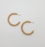 Flat lay of gold beaded hoop earrings on a white background, showing circular design with polished bead detail.