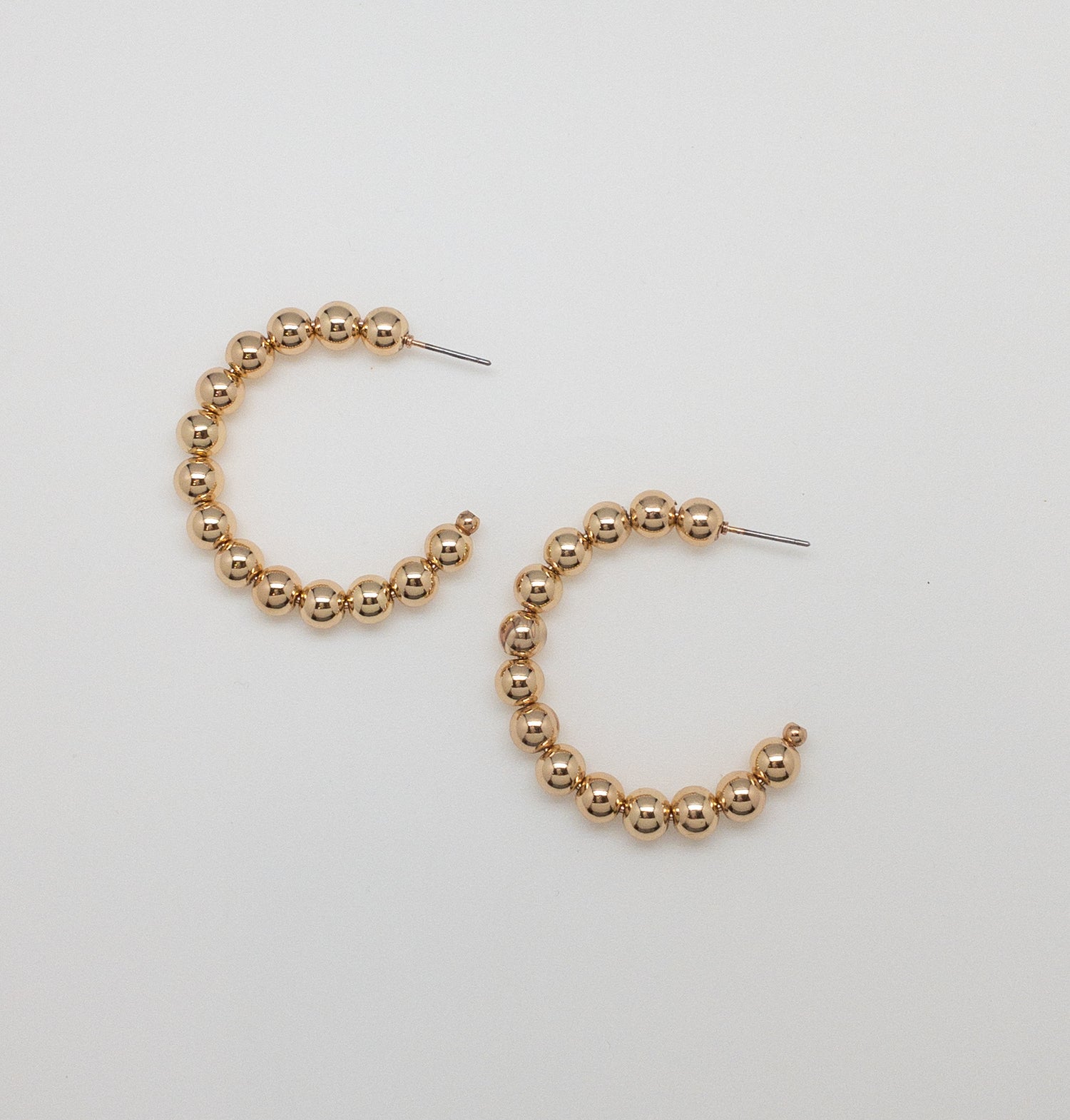 Flat lay of gold beaded hoop earrings on a white background, showing circular design with polished bead detail.