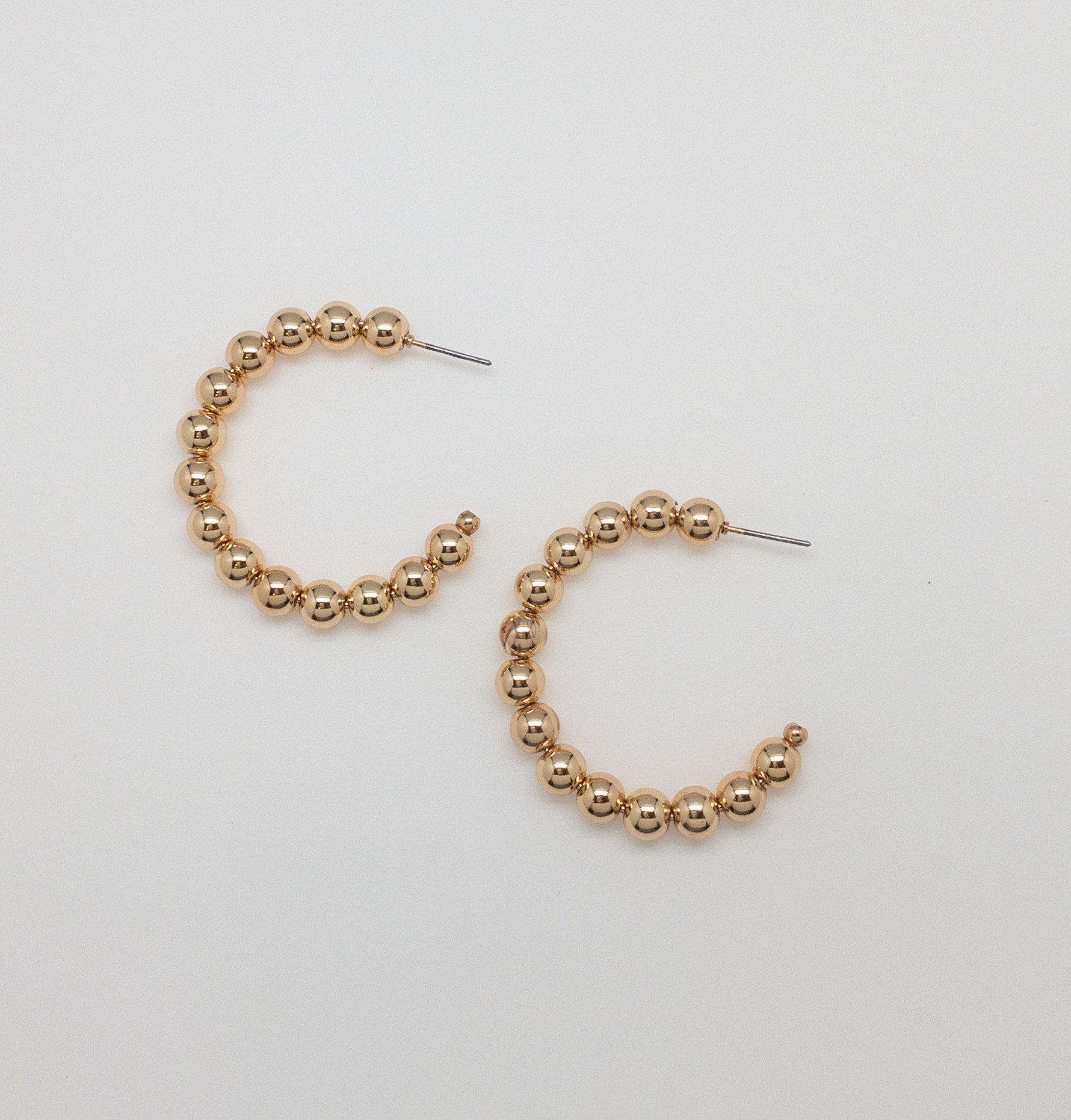 Flat lay of gold beaded hoop earrings on a white background, showing circular design with polished bead detail.