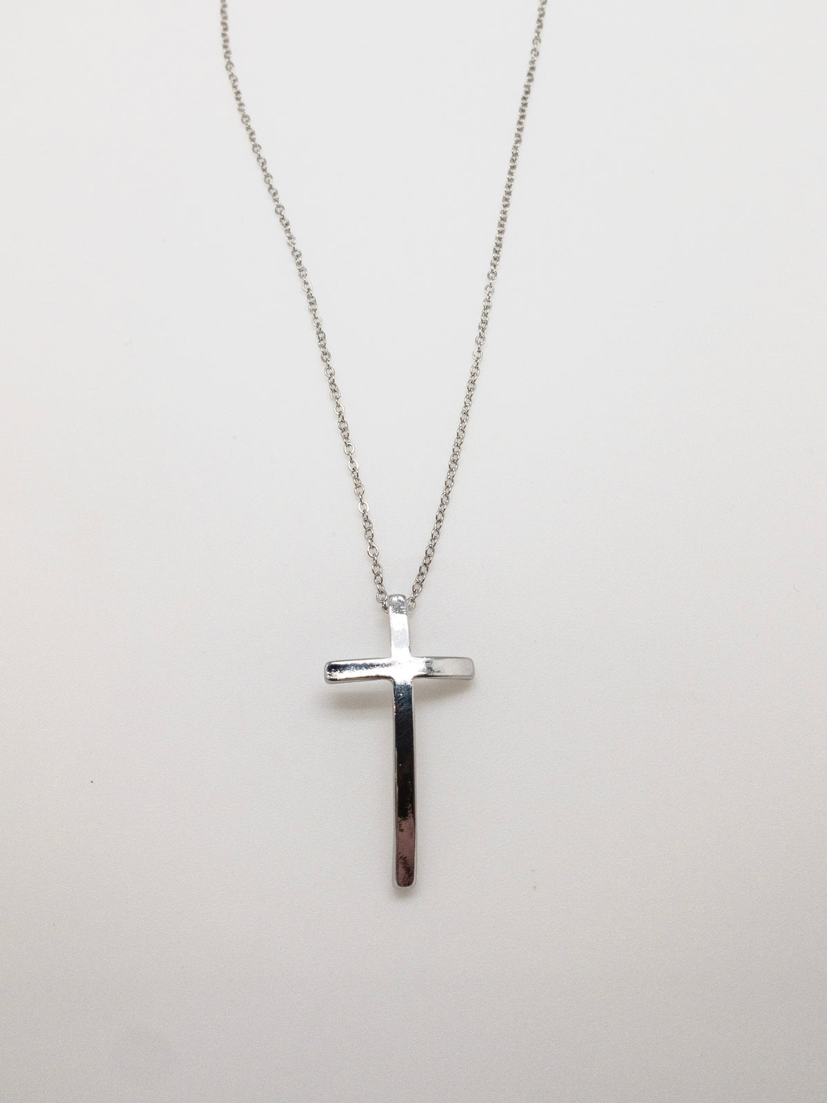 Silver-plated curved cross necklace with a delicate silver chain and slender cross pendant at Ardor Boutique.