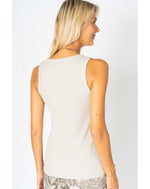 Woman wearing a white sleeveless top against a plain background