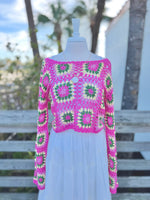 Hot pink open knit cropped floral sweater on a mannequin with a long gold necklace and a white skirt