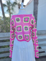 Back view of a hot pink open knit cropped floral sweater on a mannequin with a gold necklace and a white skirt
