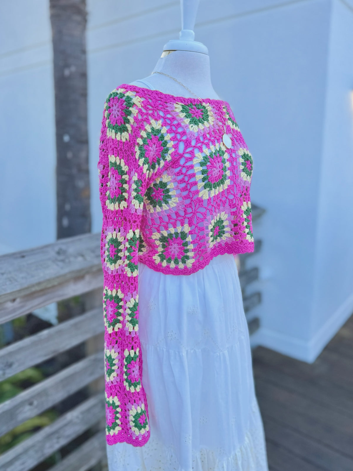 side view of a hot pink open knit cropped floral sweater on a mannequin with a long gold necklace and a white skirt