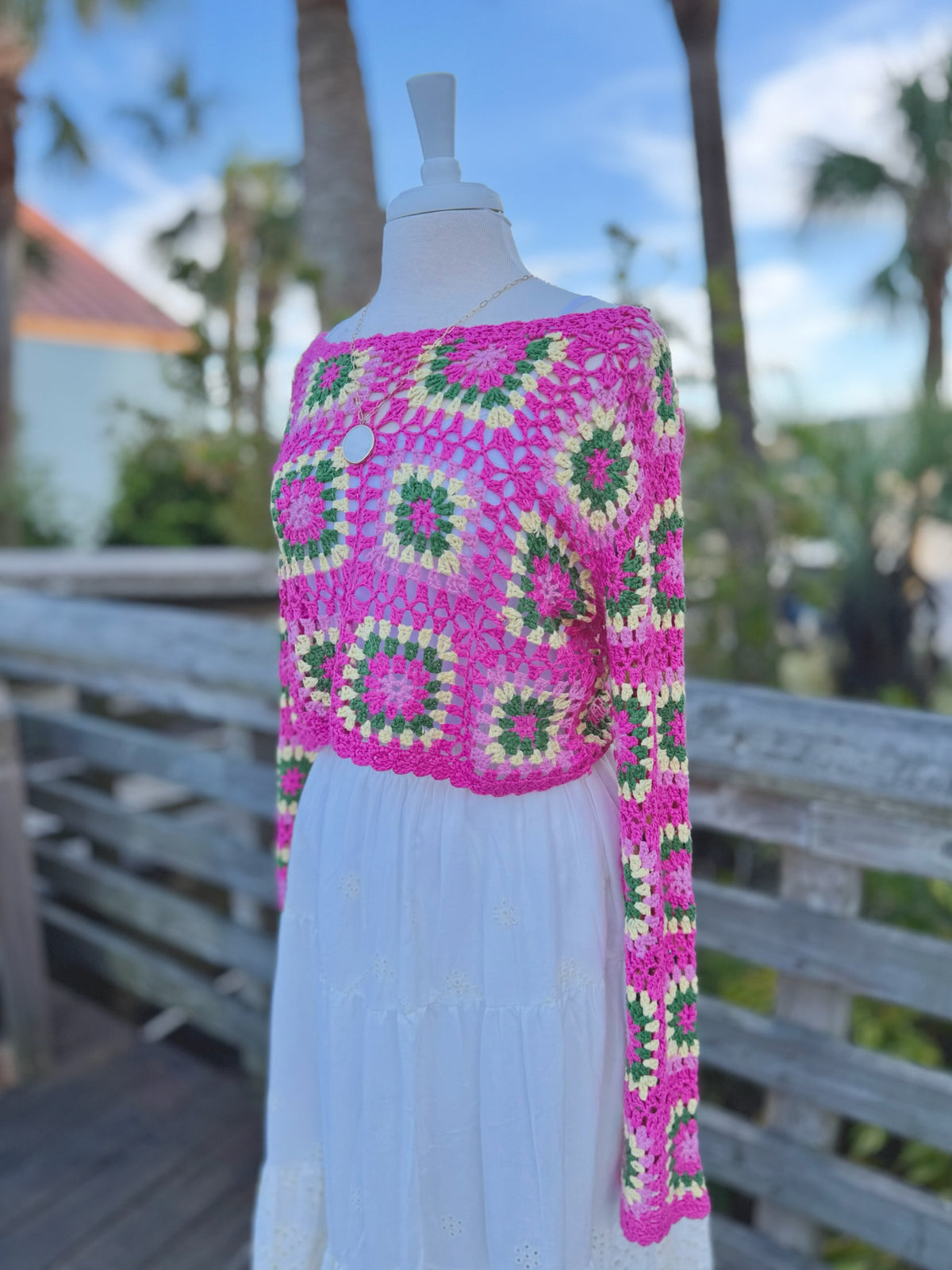 side view of a hot pink open knit cropped floral sweater on a mannequin with a long gold necklace and a white skirt