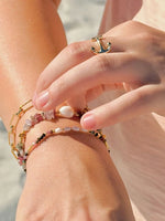 Close-up of a hand wearing the anchor ring and multiple beaded bracelets on a blurred beach background