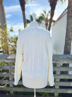 Back view of Cable Knit sweater in ivory on a mannequin outdoors.