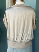 Beige silk top on a mannequin against a blue wall