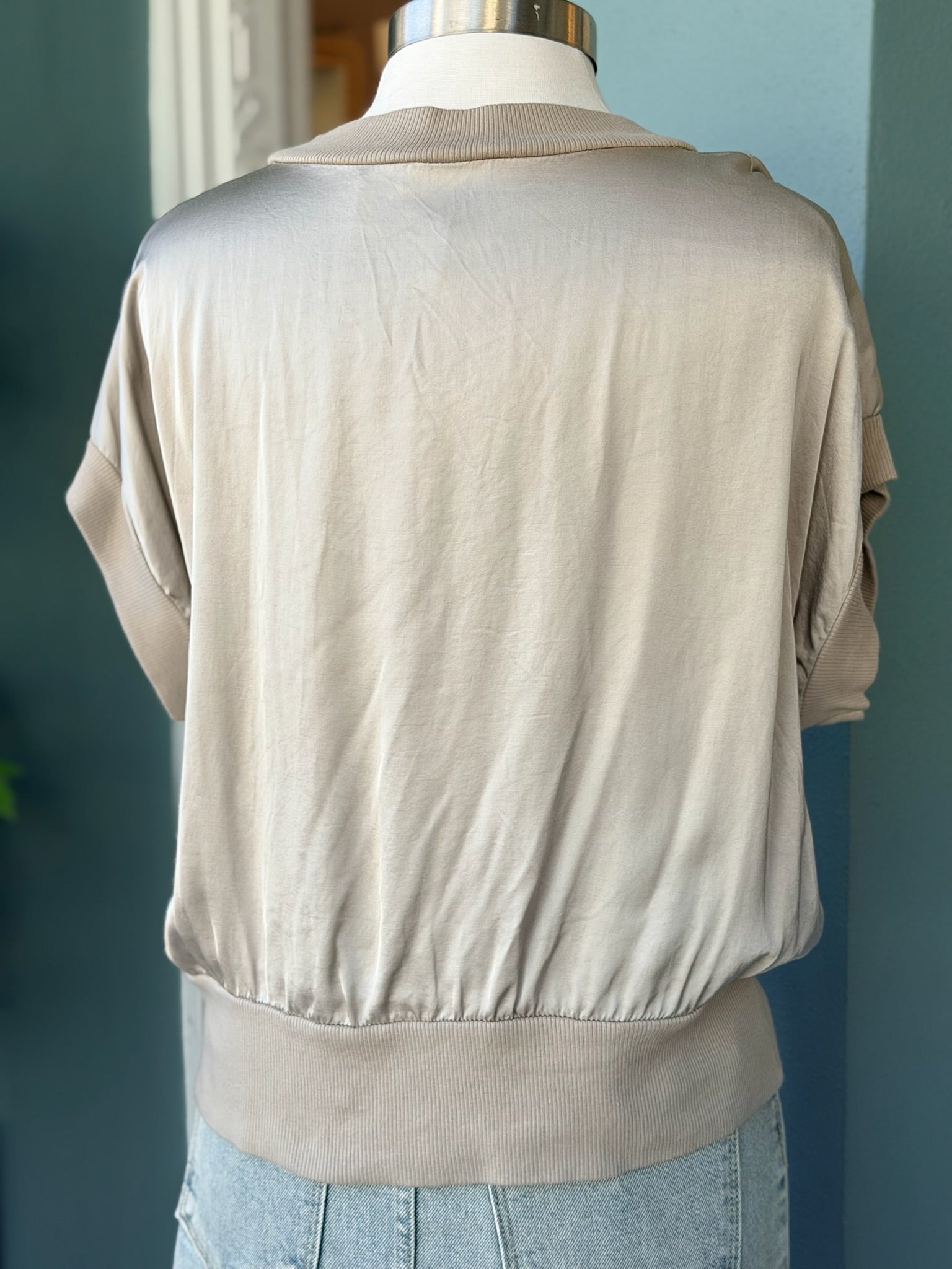 Beige silk top on a mannequin against a blue wall