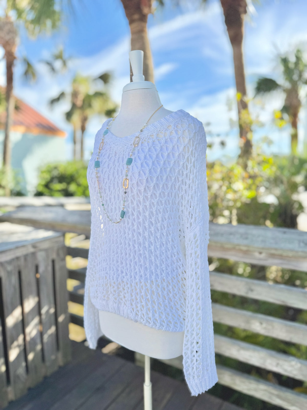 White open knit sweater on a mannequin outdoors side view with a long blue and gold necklace