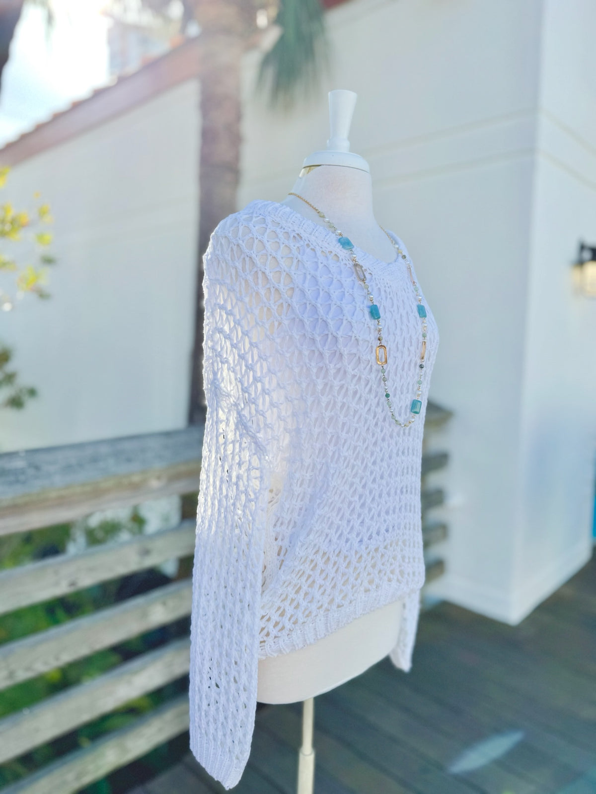 White open knit sweater on a mannequin outdoors side view with a long blue and gold necklace