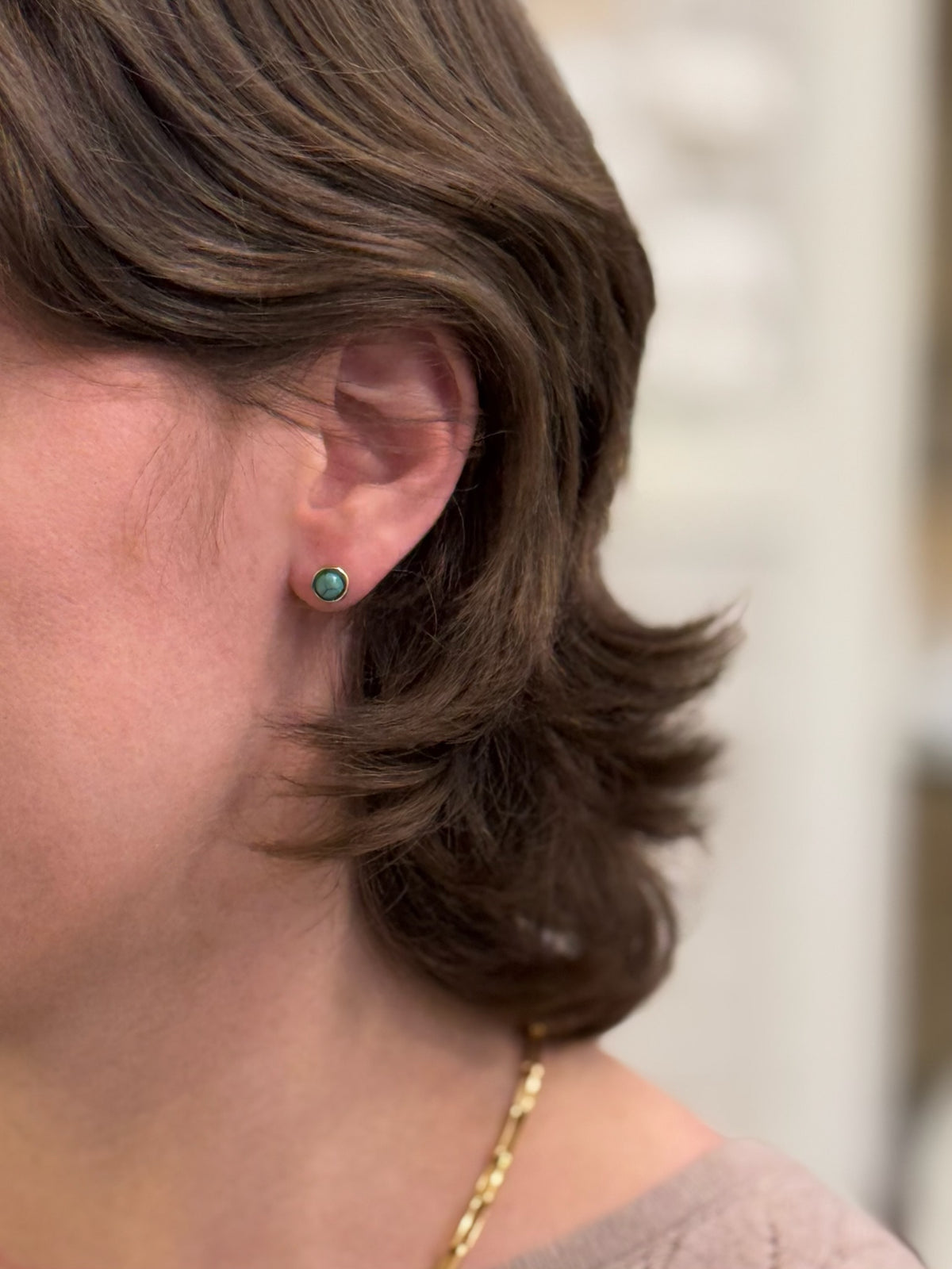 A pair of round stud earrings with blue stones being worn.