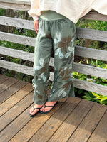 Green floral linen pants featuring frayed seams and a comfortable pull-on waistband, worn with a cream top and black sandals.