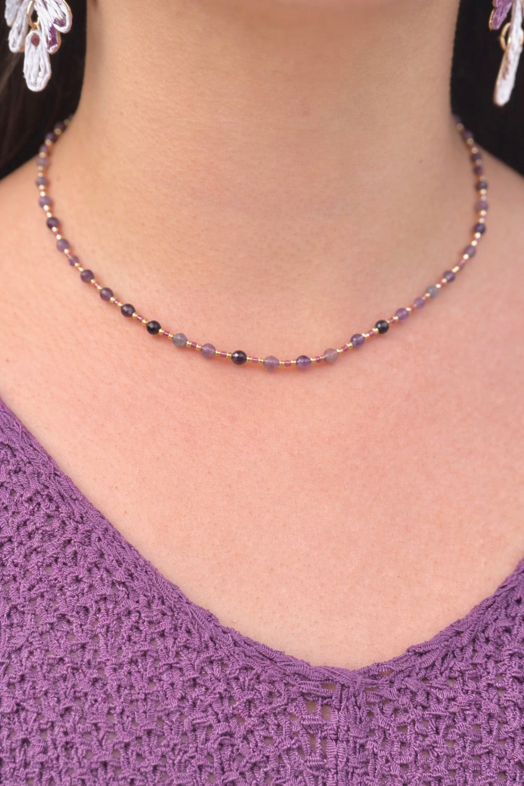 Necklace with purple and black beads worn by a person in a purple top.