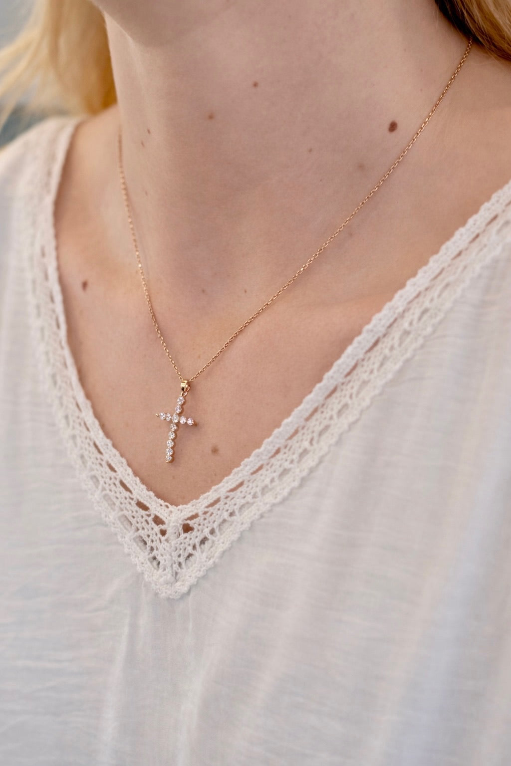 Gold necklace with a cross pendant worn by a person in a white lace top.
