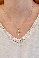 Rose gold necklace with a cross pendant worn by a person wearing a white lace top.