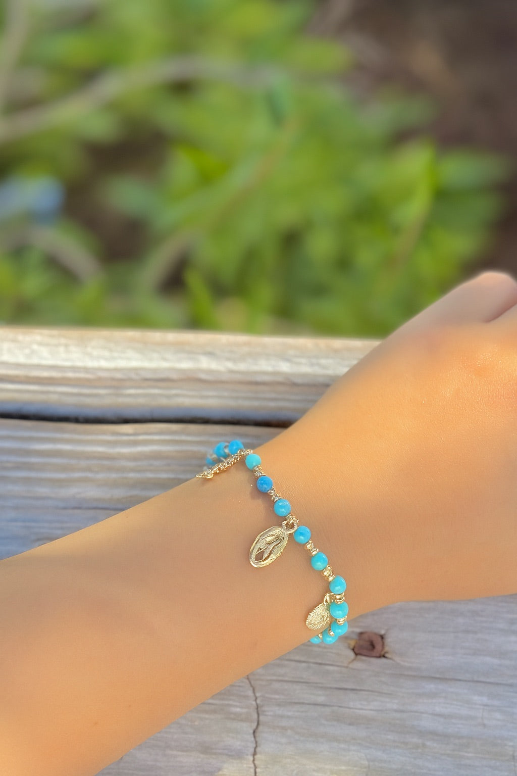Hand wearing a turquoise beaded bracelet with gold accents on a wooden surface.
