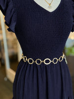 Gold circular link chain belt with smooth and textured rings styled at the waist over a navy dress at Ardor Boutique.