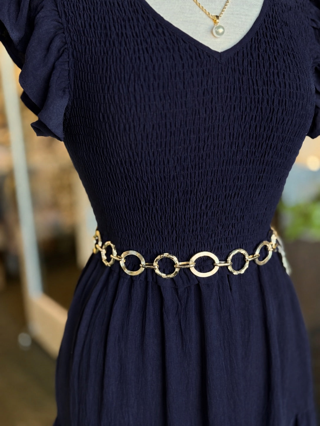 Gold circular link chain belt with smooth and textured rings styled at the waist over a navy dress at Ardor Boutique.