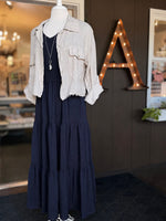 Navy maxi dress with a smocked bodice, V-neckline, ruffle short sleeves and a flowing tiered skirt paired with a beige linen jacket at Ardor Boutique.