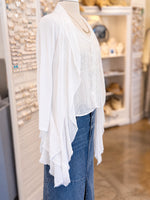 A white lace-trimmed long-sleeve cardigan layered over a white lace blouse and paired with a blue denim skirt, displayed on a mannequin torso inside a retail store.