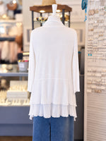 Back view of a  white lace-trimmed long-sleeve cardigan layered paired with a blue denim skirt, displayed on a mannequin torso inside a retail store.