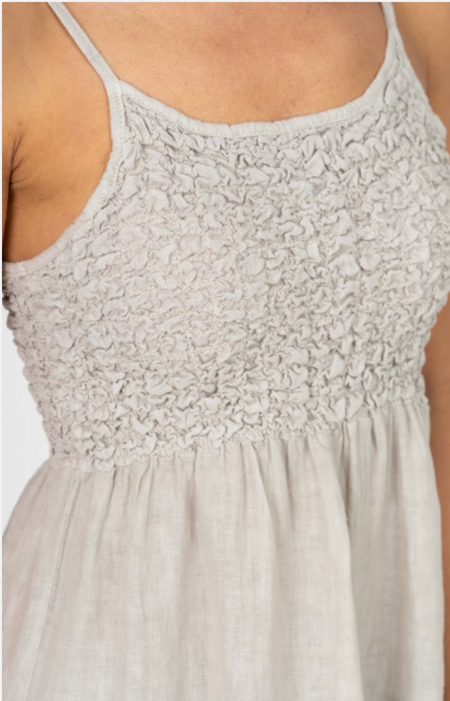 Close-up of cream sleeveless tiered dress showing textured bodice and thin straps