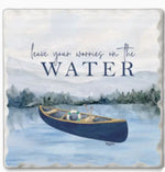 Square decorative coaster featuring a watercolor lake scene with a canoe on the water and the phrase “leave your worries on the WATER” in dark blue lettering.