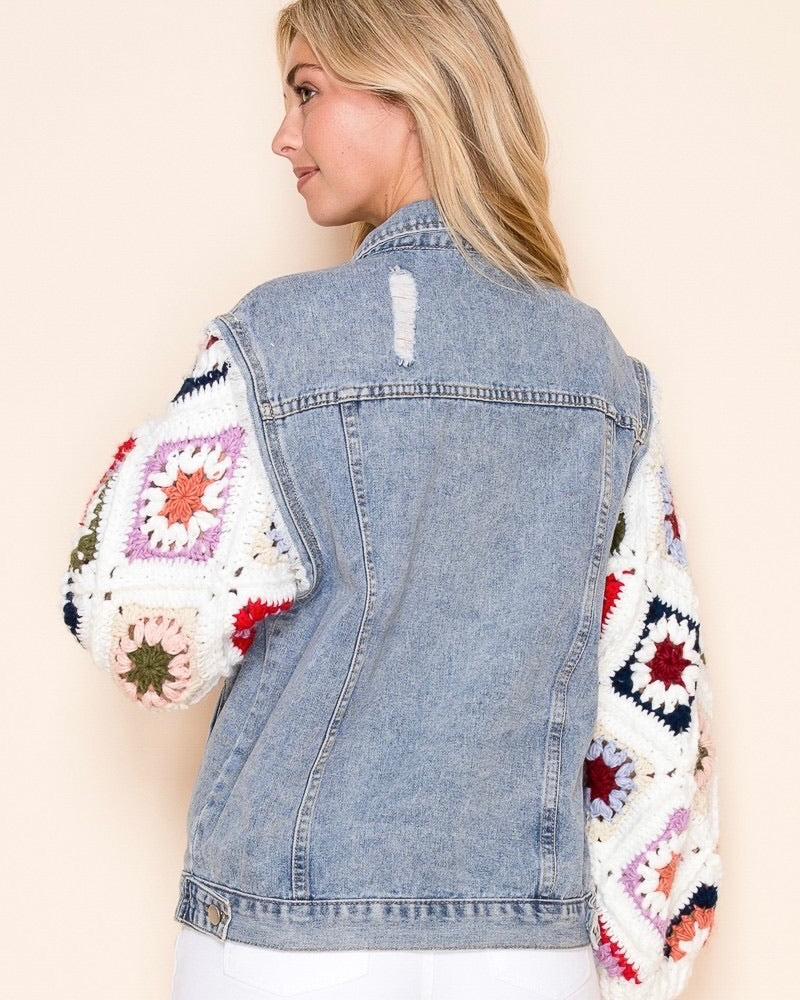 Back view of a model wearing the oversized Dahlia Granny Square Denim Jacket with light wash distressed denim and colorful hand-crocheted granny square sleeves.