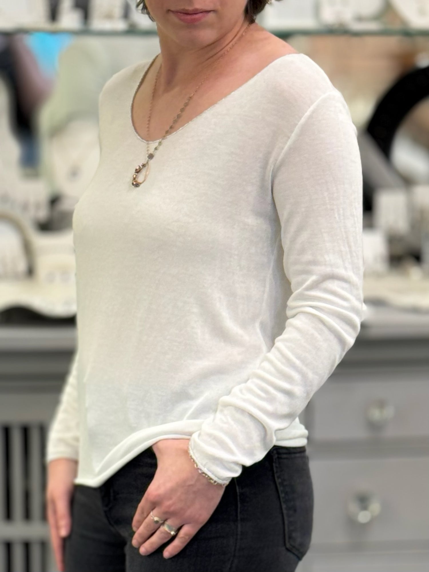 Woman wearing a soft white long sleeve knit top with a rounded neckline, shown from a side angle.