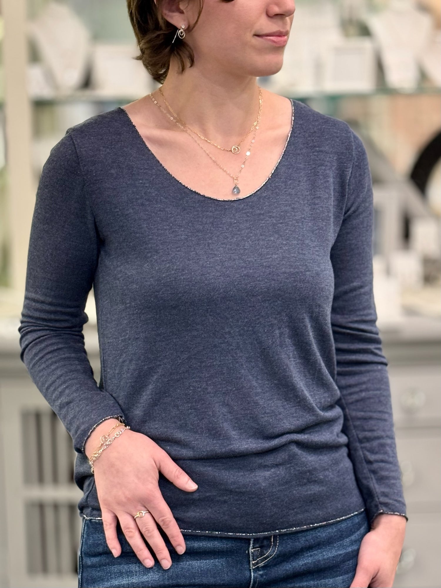 Woman wearing a navy long sleeve knit top with a scoop neckline and fitted silhouette, styled with denim jeans and layered gold necklaces.