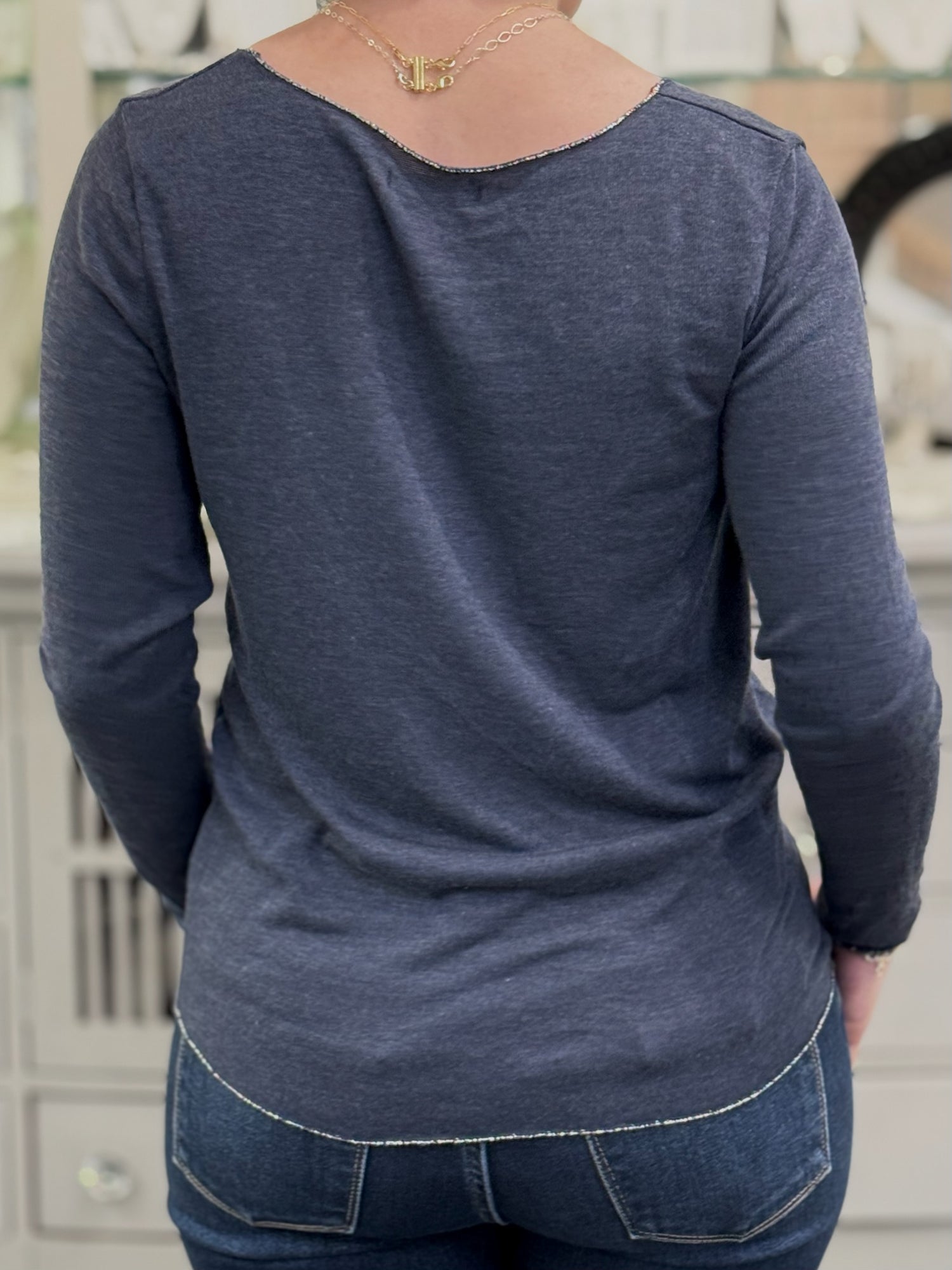 Back view of a lightweight navy knit top with curved hem and fine texture, worn with medium-wash jeans.