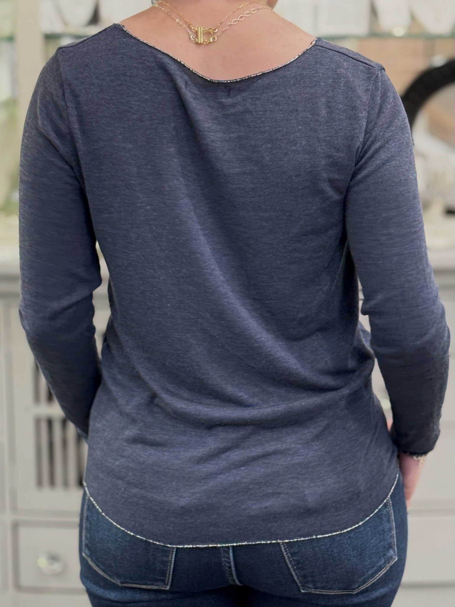 Back view of a lightweight navy knit top with curved hem and fine texture, worn with medium-wash jeans.