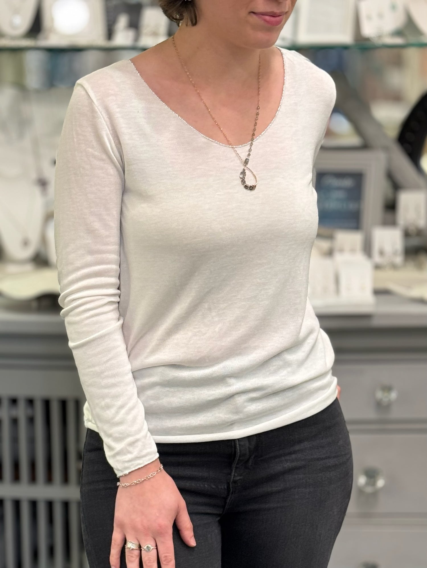 Woman wearing a lightweight white long sleeve top featuring a scoop neckline and subtle sheer texture.
