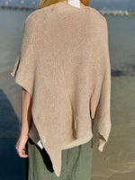 Back view of the Elise Wrap Poncho in Beige featuring a textured knit, relaxed drape, and asymmetrical hem, styled with olive green pants at Ardor Boutique.