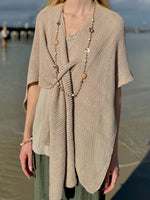 Front view of the Elise Wrap Poncho in Beige featuring a textured knit, soft draping, and front tie detail, styled with a long beaded necklace at Ardor Boutique.
