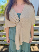Woman wearing a gold knitted shawl over a green dress with a blurred outdoor background