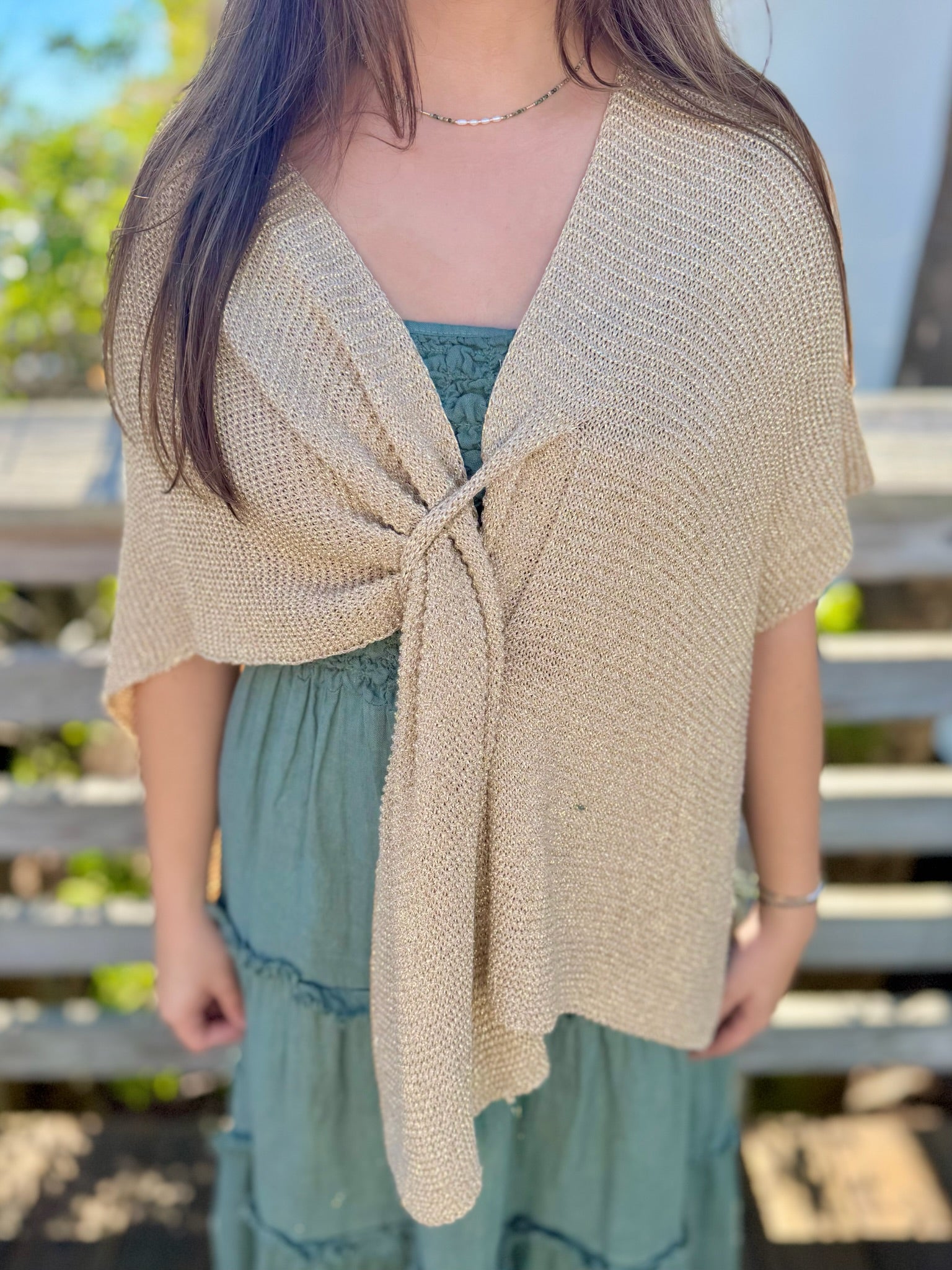 Woman wearing a gold knitted shawl over a green dress with a blurred outdoor background