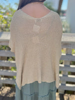 Beige knit top worn by a person with a blurred outdoor background