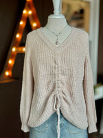 Soft beige textured sweater on mannequin with V neck and adjustable drawstring in front, styled with denim and a beaded necklace.