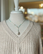 Close up of neutral textured sweater V neck showing the knit detail and a beaded lariat necklace with a single pearl drop.