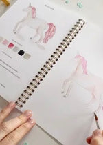 Open Fairytale watercolor workbook showing unicorn watercolor lesson with guided instructions and sketch ready to paint on thick paper