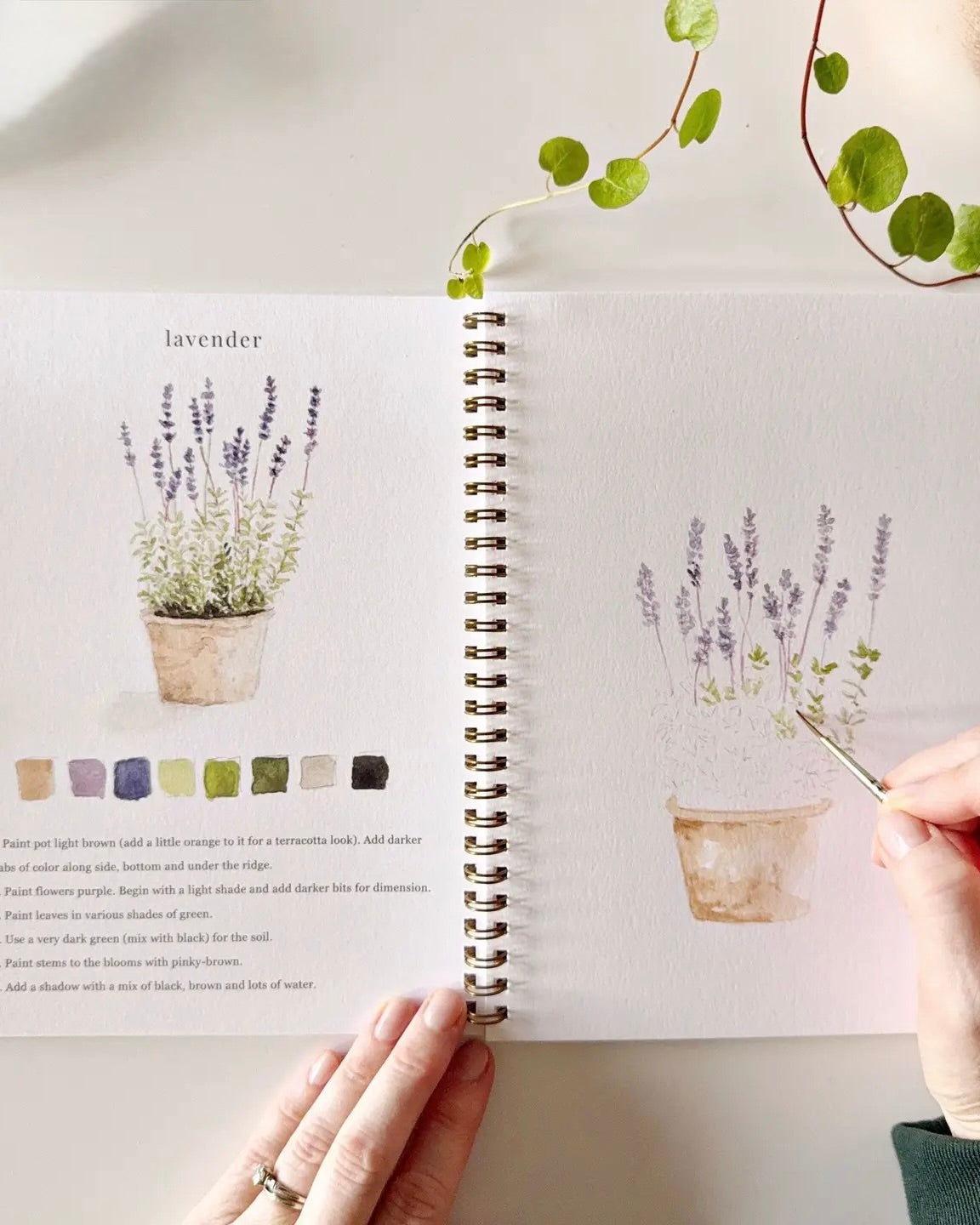 Open Garden watercolor workbook by Emily Lex showing a lavender watercolor lesson with prompts and an in progress painting on thick watercolor paper