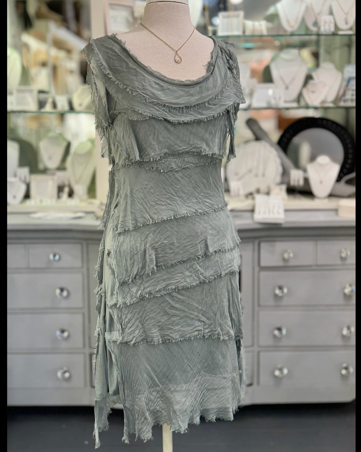 Gianna Italian silk dress in olive displayed on a mannequin at Ardor Boutique, featuring a scoop neckline, asymmetrical silk tiers, and frayed trim.